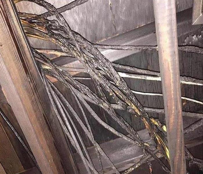 upward view of attic crawlspace blackened by fire with damaged electrical cables